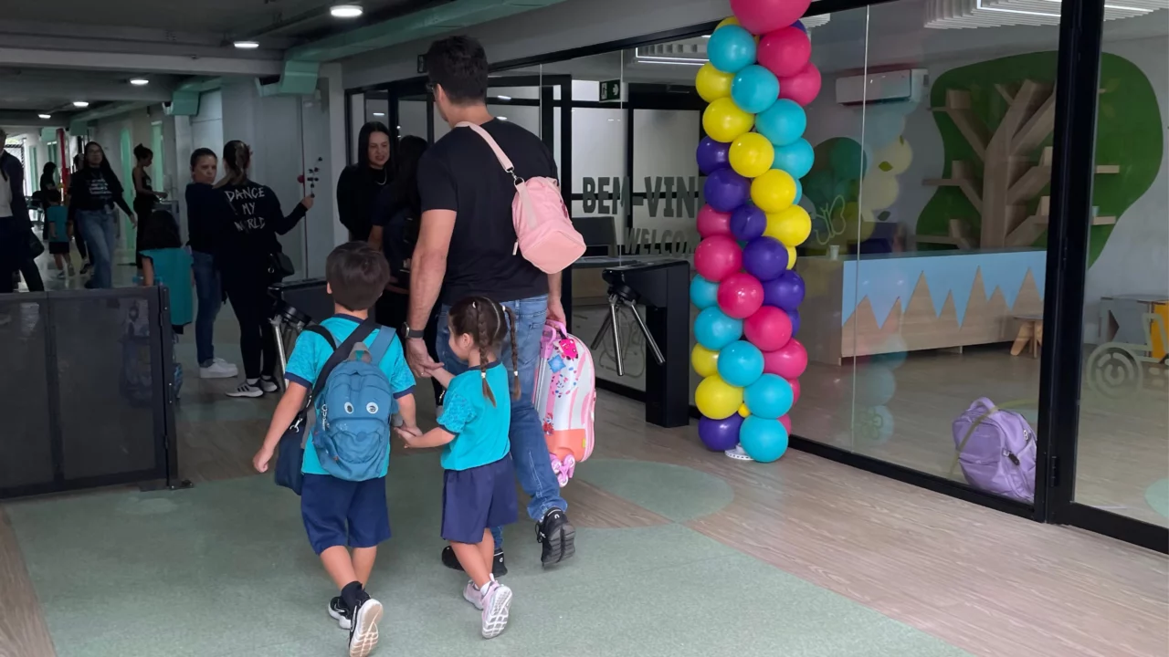 Pai e filhos de mãos dados entrando na escola no volta às aulas.